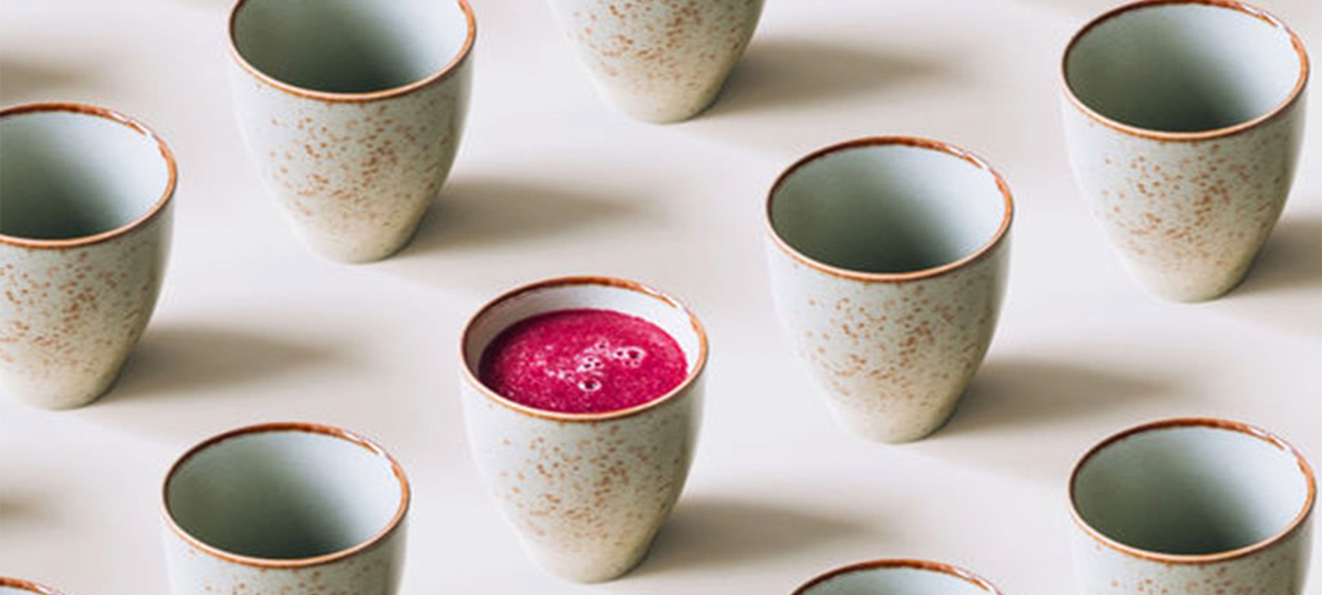 A row of Japanese inspired ceramic mugs with one mug containing pink juice