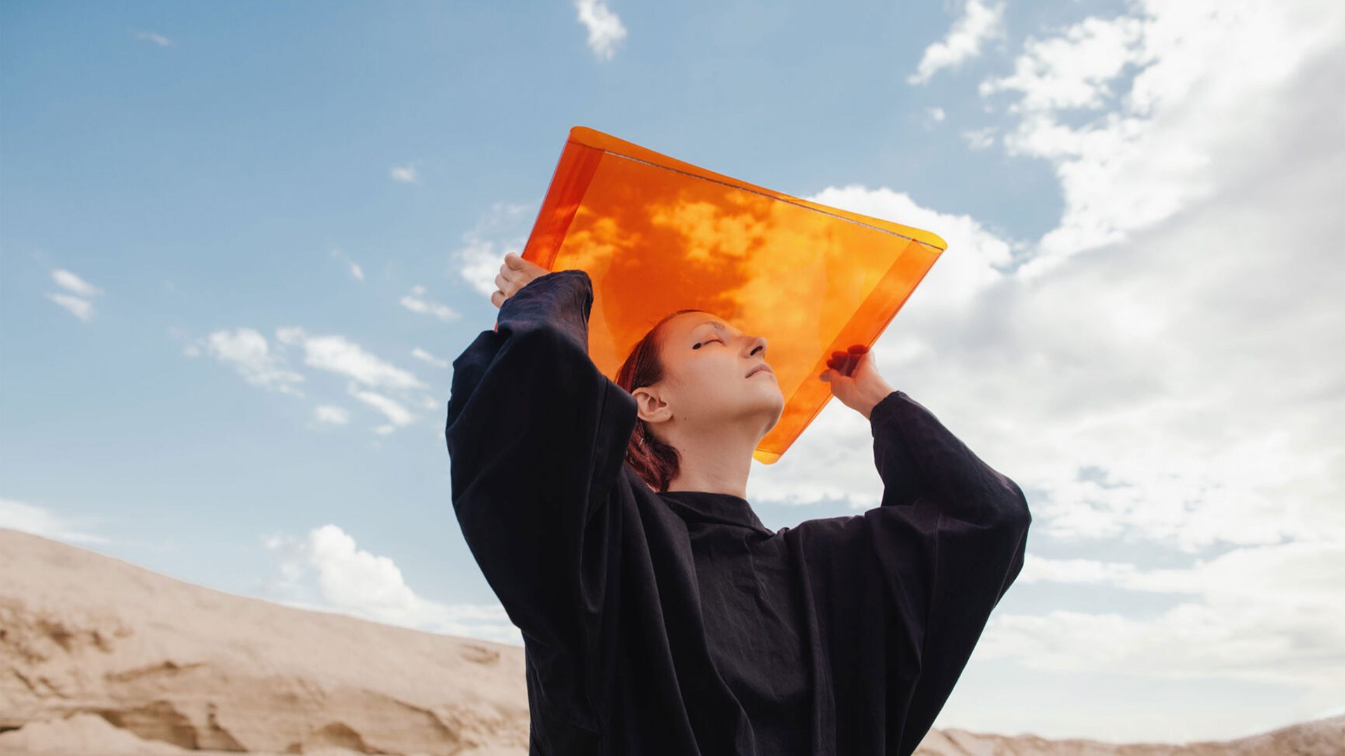 Girl holds up orange sheet against a blue sky