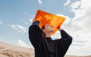 Girl holds up orange sheet against a blue sky