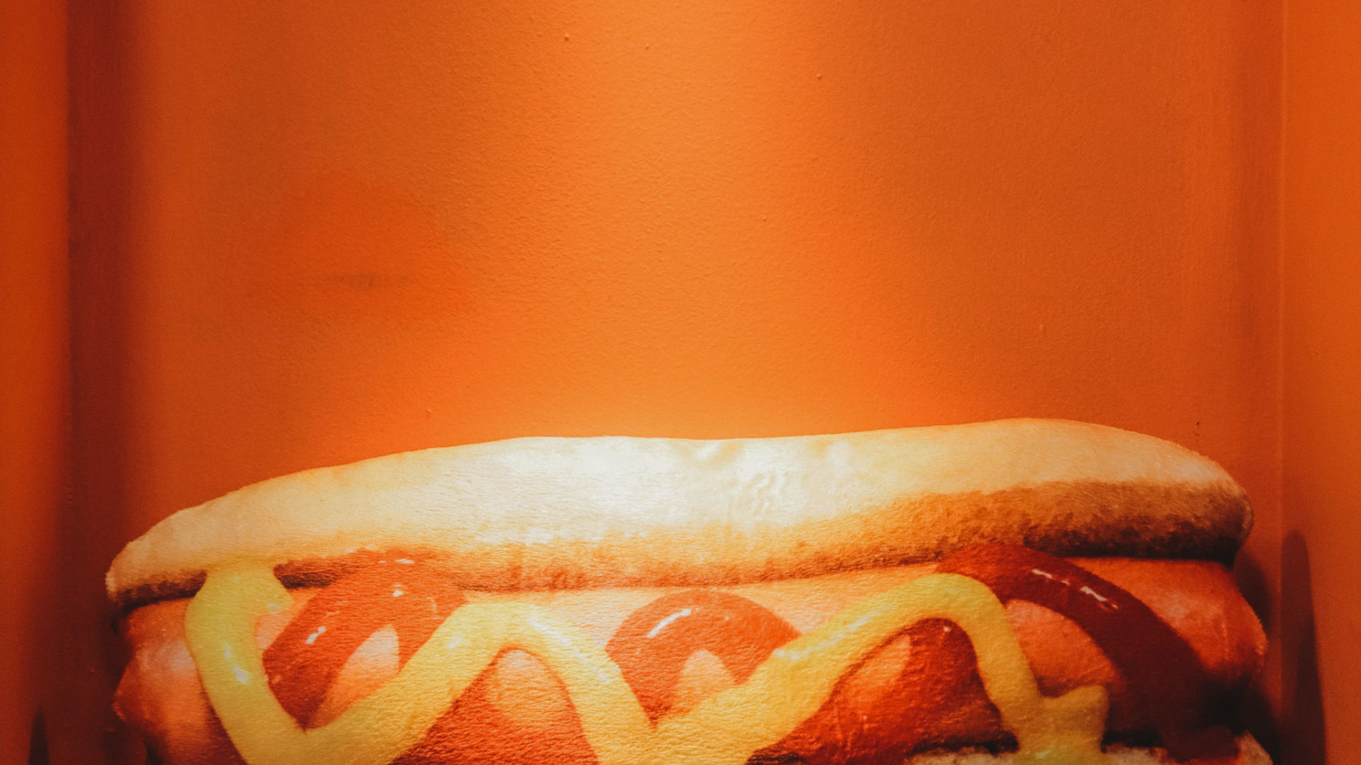 Hot dog with ketchup and mustard on orange background