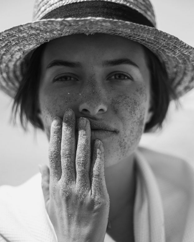 Black and white photograph of model wearing a sun hat holding her face